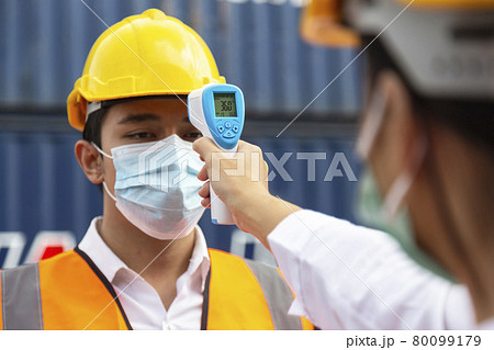 asian man worker wearing face mask checking fever by digital thermometer before entering the work for protecting from covid, covid-19 or coronavirus pandemic on construction site. selective focus. 80099179