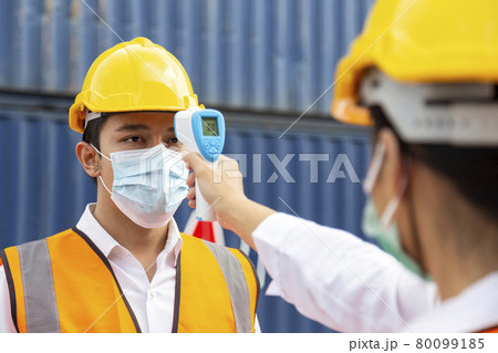 asian man worker wearing face mask checking fever by digital thermometer before entering the work for protecting from covid, covid-19 or coronavirus pandemic on construction site. selective focus. asian man worker wearing face mask checking fever by digital thermometer before entering the work for protecting from covid, covid-19 or coronavirus pandemic on construction site. selective focus. 80099185