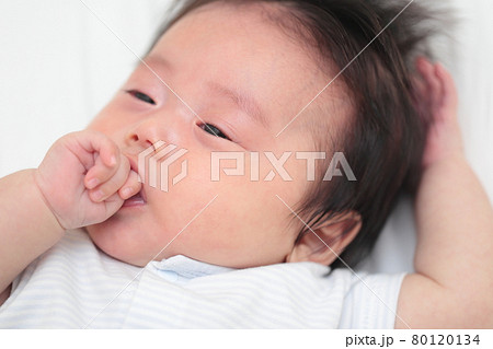 ベッドで寝転んで指しゃぶりをする赤ちゃんの女の子 ベッドで寝転んで指しゃぶりをする赤ちゃんの女の子 80120134