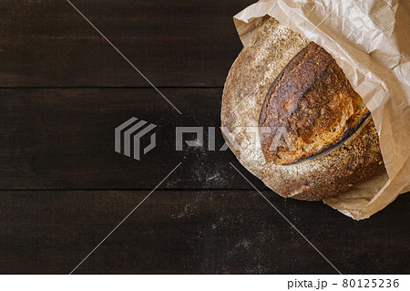 Homemade wheat bread on dark wooden background with particles of flour. Top view of crispy baked bread surface texture 80125236