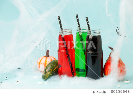 Halloween drink. Black Red Green cocktail in glass jar decorated with straws, pupmkins on blue, creative idea for Home party, funny food, spooky toxic drink for kids, seasonal menu Halloween drink. Black Red Green cocktail in glass jar decorated with straws, pupmkins on blue, creative idea for Home party, funny food, spooky toxic drink for kids, seasonal menu 80156648