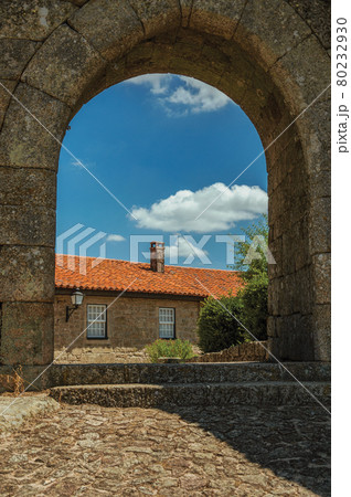 Stone house seen through wall gate arch 80232930