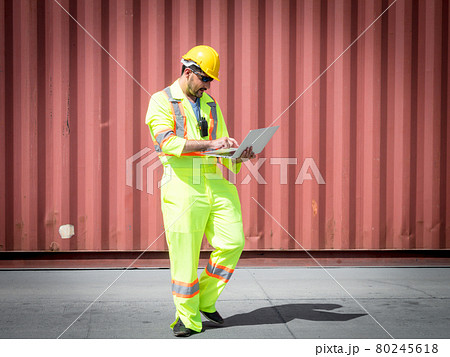 Inspection Asian engineer is using a laptop computer and wearing a yellow safety helmet and check for control loading containers box from Cargo freight ship for import and export.. 80245618