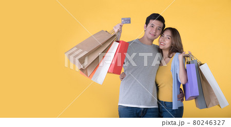 Asian couple holding credit card and shopping bags isolated on yellow background 80246327