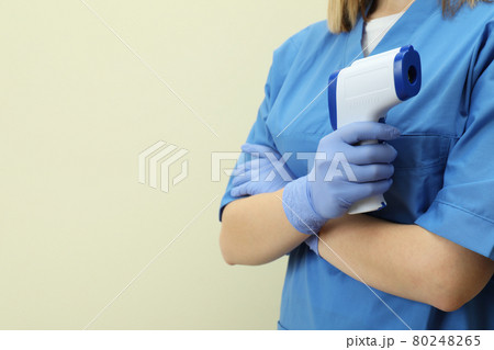 Female doctor hold thermometer gun on beige background 80248265