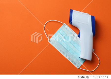 Thermometer gun and medical mask on orange background 80248274