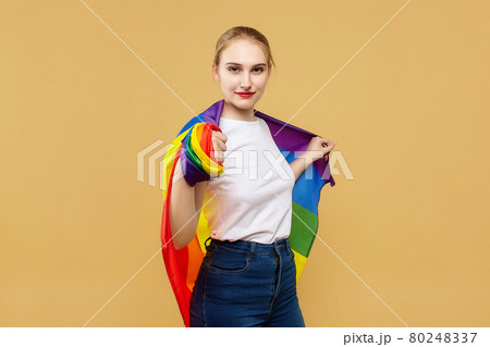 attractive blonde made posing with a rainbow LGBT flag. photo shoot in the studio on a yellow background attractive blonde made posing with a rainbow LGBT flag. photo shoot in the studio on a yellow background 80248337