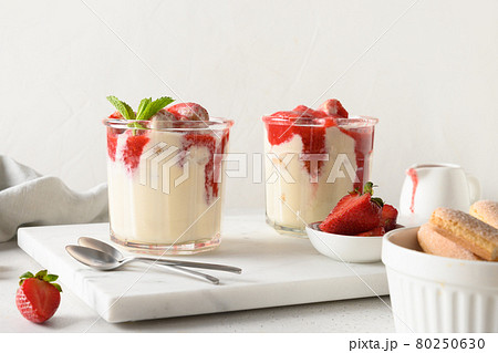 Layered dessert in glass jars with cookie savoyardi, mascarpone and whipped cream decorated strawberries Layered dessert in glass jars with cookie savoyardi, mascarpone and whipped cream decorated strawberries 80250630