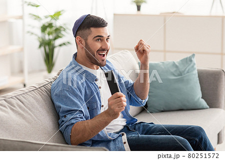Happy jewish guy spending weekend watching tv shaking clenched fists Happy jewish guy spending weekend watching tv shaking clenched fists 80251572