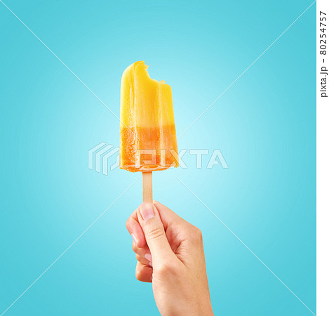 Bitten red frozen fruit ice cream popsicle in woman hand on blue background Bitten red frozen fruit ice cream popsicle in woman hand on blue background 80254757