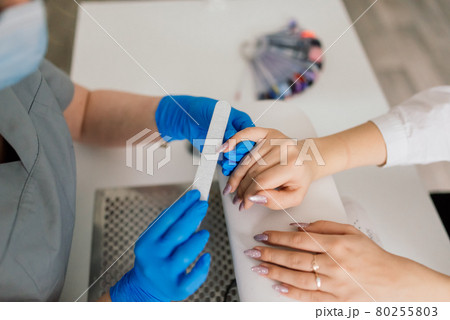 Manicurist wearing protective mask painting female nails with nail polish in a manicure salon. Manicurist wearing protective mask painting female nails with nail polish in a manicure salon. 80255803