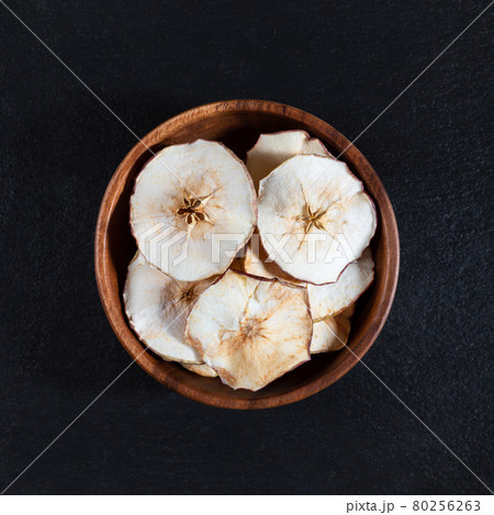 Dried Apple chips in a wooden bowl on a black stone background. Organic natural food. Dried Apple chips in a wooden bowl on a black stone background. Organic natural food. 80256263