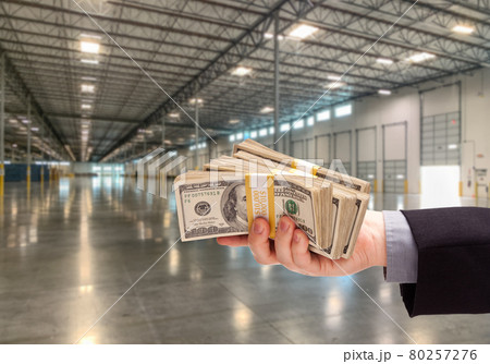Male Hand Holding Thousands of Dollars Inside Empty Industrial Warehouse. Male Hand Holding Thousands of Dollars Inside Empty Industrial Warehouse. 80257276