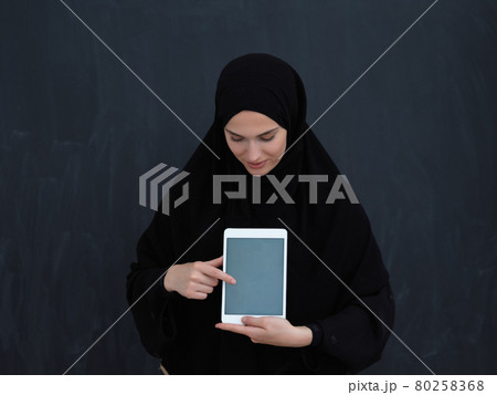 Young Arab businesswoman in traditional clothes or abaya and glasses showing tablet computer display Young Arab businesswoman in traditional clothes or abaya and glasses showing tablet computer display 80258368