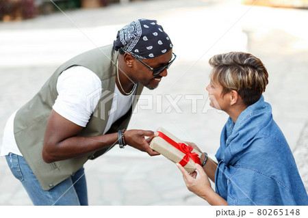 Happy middle age interracial couple sitting . Man giving Valentine's day gift to his woman,girlfriend or wife.  80265148