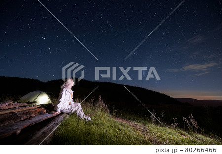 Young woman sitting near tent in mountains. 80266466