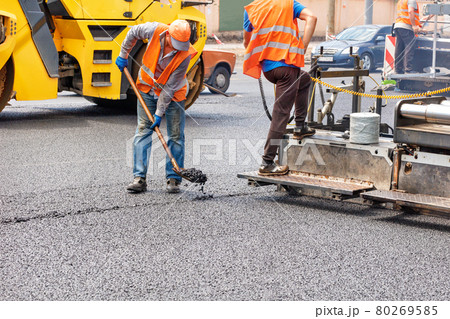 A team of road workers is laying fresh asphalt with industrial road machinery. A team of road workers is laying fresh asphalt with industrial road machinery. 80269585