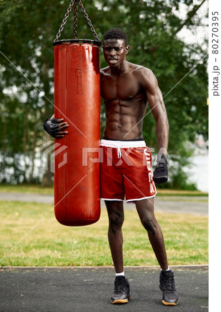An African American athlete boxing outdoors. An African American boxing a bag in the park on the playground. 80270395
