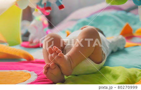 A newborn baby lies on its back on a bright developing rug with toys and explores its surroundings 80270999