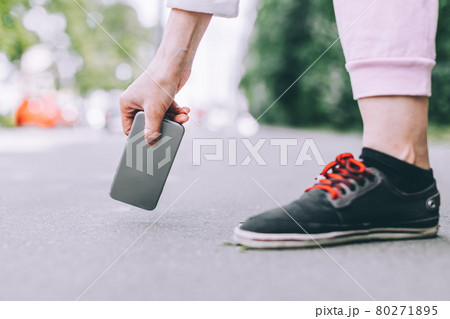 Young woman picks up from the asphalt fallen not crashed smartphone. 80271895