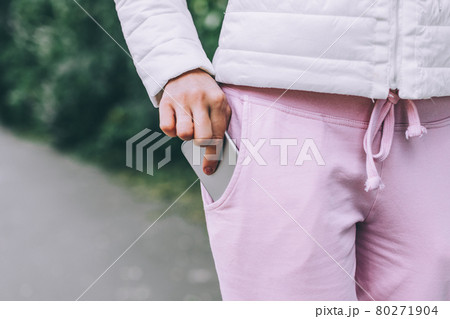 Woman's hand put smartphone in not zippered pocket on pants. Danger of dropping. 80271904