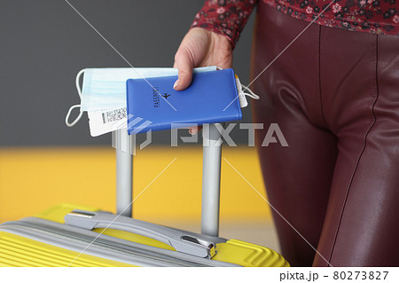 Woman holding passport, plane ticket, medical mask and suitcase Woman holding passport, plane ticket, medical mask and suitcase 80273827