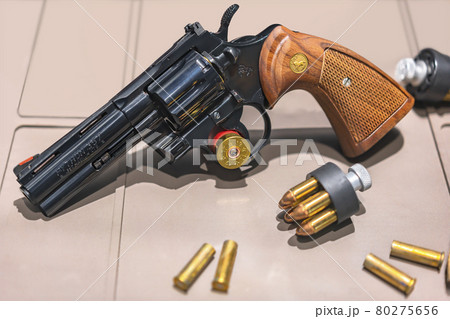 弾丸で聳えたスピードローダーとリボルバーのコルトパイソン357マグナムのレプリカ。 80275656