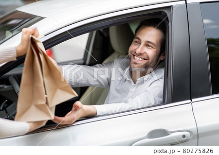 Food delivery courier gives paper bags to man in car. Safety food delivered Food delivery courier gives paper bags to man in car. Safety food delivered 80275826