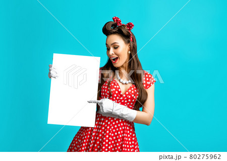 Excited pinup retro style woman pointing at empty advertising banner with copy space on blue studio background, mockup Excited pinup retro style woman pointing at empty advertising banner with copy space on blue studio background, mockup 80275962