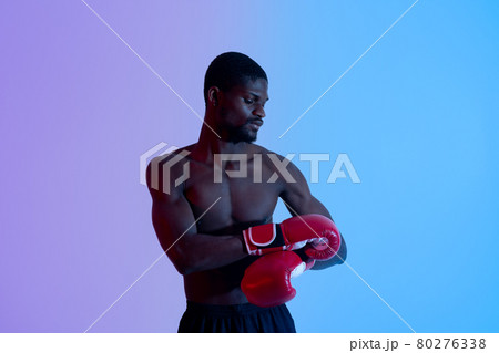 Professional young black boxer with bare torso putting on or taking off red gloves in neon lighting Professional young black boxer with bare torso putting on or taking off red gloves in neon lighting 80276338