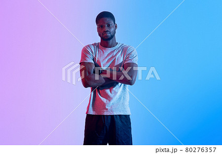 Black male fitness model standing with crossed arms, looking at camera in neon light 80276357
