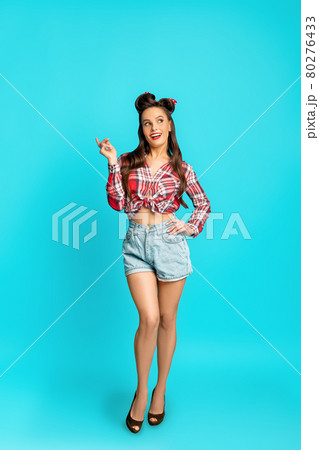 Full length portrait of playful happy pinup woman in retro style wear posing over blue studio background 80276433