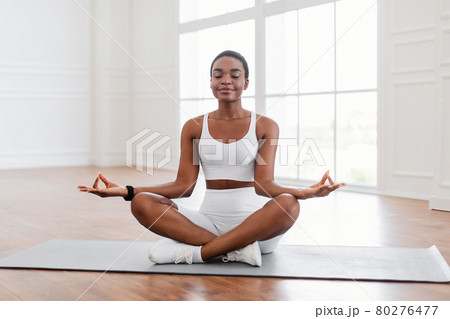 Young black woman sitting in lotus position on mat, meditating Young black woman sitting in lotus position on mat, meditating 80276477