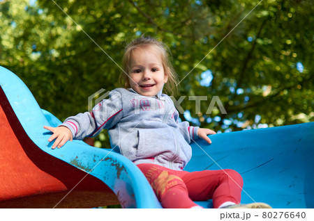 Cute little girl having fun while sliding down a playground slide 80276640