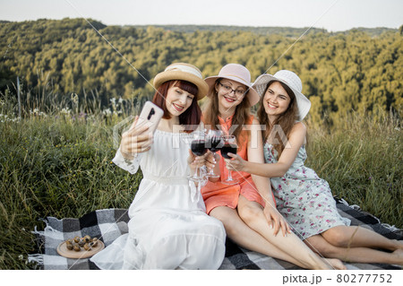 female friends, enjoying summer picnic and toasting wine glasses, making selfie photo on smartphone 80277752