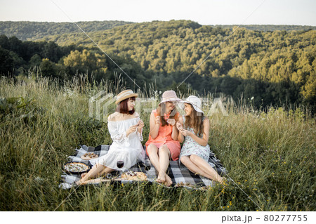 Three attractive girls holding escargot snails in hands and eating, against the background of green hills 80277755