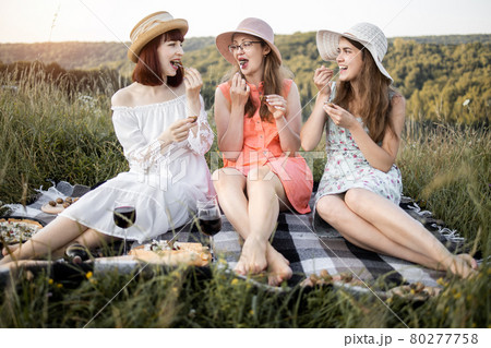 Three attractive girls holding escargot snails in hands and eating, against the background of green hills 80277758