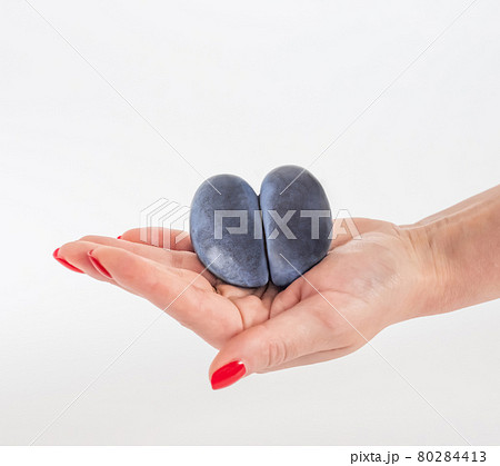 Trendy ugly food concept. Purple ugly plum in a woman's hand on a white background. Fruit with heart shape. The problem of food waste Trendy ugly food concept. Purple ugly plum in a woman's hand on a white background. Fruit with heart shape. The problem of food waste 80284413