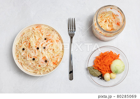 Homemade sauerkraut. Fermented food. Sauerkraut with carrots in a bowl and glass jar on a concrete white background. Vertical orientation. Homemade sauerkraut. Fermented food. Sauerkraut with carrots in a bowl and glass jar on a concrete white background. Vertical orientation. 80285069