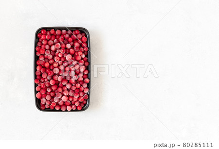 Frozen berries in a black plastic container on a white background. Vitamins. Frozen food. Copy space, top view. 80285111