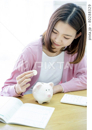 貯金箱にお金を入れる女性 80288329