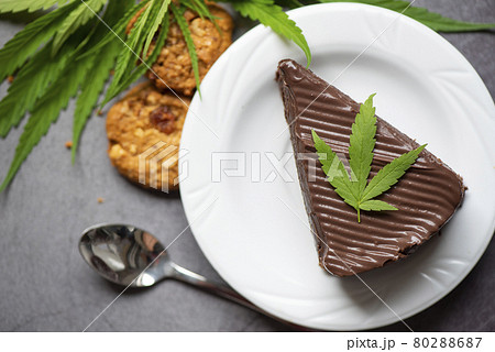 Chocolate cake and cookies with cannabis leaf - marijuana leaves plant on white plate on the wooden table, cannabis food nature herb concept Chocolate cake and cookies with cannabis leaf - marijuana leaves plant on white plate on the wooden table, cannabis food nature herb concept 80288687