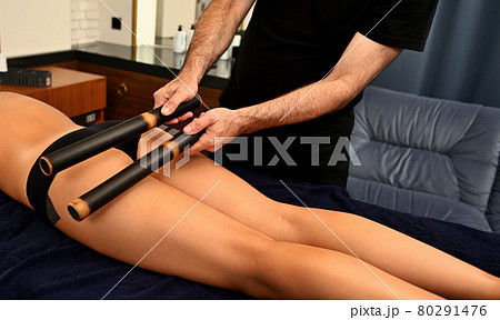 Ayurvedic bamboo stick massage performed by professional masseur on woman's body in spa resort Ayurvedic bamboo stick massage performed by professional masseur on woman's body in spa resort 80291476