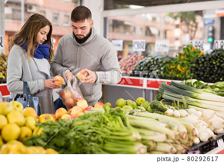 Friendly couple examining apples in grocery shop Friendly couple examining apples in grocery shop 80292617