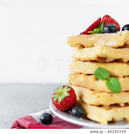 Stack of Belgian waffles, blueberry, strawberry cuts, mint leaf, sugar powder Stack of Belgian waffles, blueberry, strawberry cuts, mint leaf, sugar powder 80293349