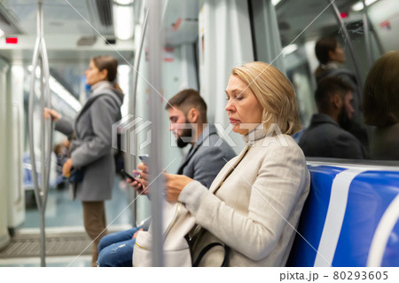Adult woman browsing and typing messages on tablet in subway car leaning on handrail 80293605