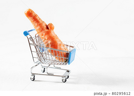 Trendy ugly food concept. Funny carrot in toy grocery cart on white background. Vegetable with a strange shape. The problem of food waste. Trendy ugly food concept. Funny carrot in toy grocery cart on white background. Vegetable with a strange shape. The problem of food waste. 80295612