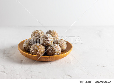 Homemade energy balls with dried apricots, raisins, dates, walnuts, almonds and coconut. Healthy sweet food. Energy balls in a wooden plate on a white background 80295632