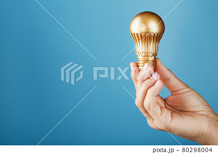 Gold light bulb in hand on a blue background, as a concept of ideas and assistance Gold light bulb in hand on a blue background, as a concept of ideas and assistance 80298004