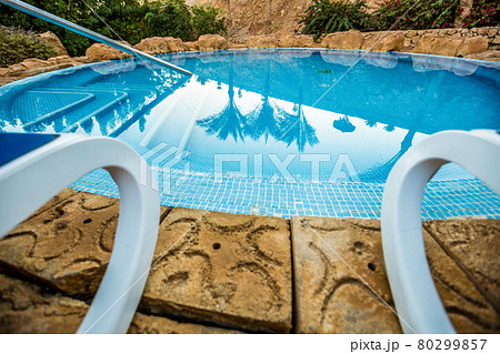 Closeup sunloungers and swimming pool with reflected palms in water 80299857